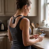 Woman checking her phone in the kitchen wearing the posture sensor